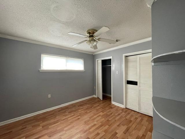 unfurnished bedroom with two closets, light wood-style flooring, ornamental molding, a textured ceiling, and baseboards