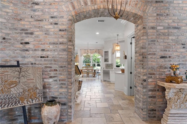 corridor with arched walkways, recessed lighting, stone tile floors, visible vents, and crown molding