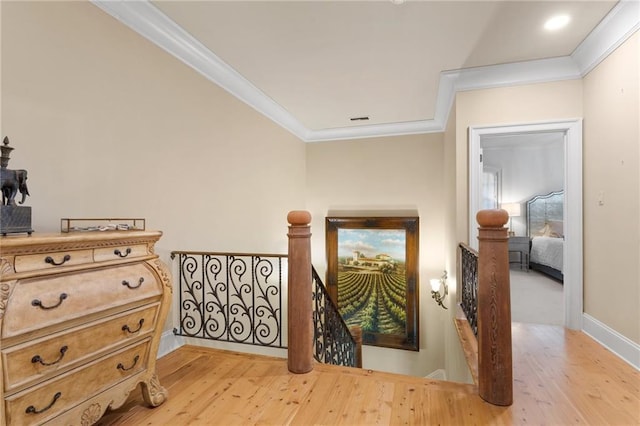 hall with ornamental molding, light wood-style flooring, and an upstairs landing