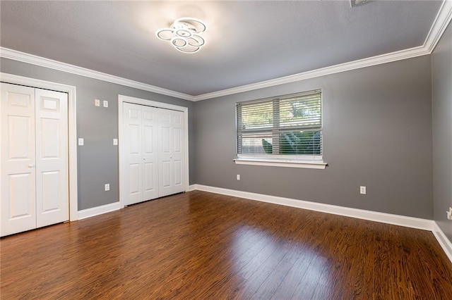 unfurnished bedroom featuring dark hardwood / wood-style flooring, two closets, and ornamental molding