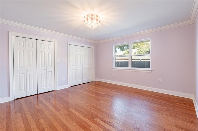 unfurnished bedroom with hardwood / wood-style floors, two closets, ornamental molding, and a notable chandelier