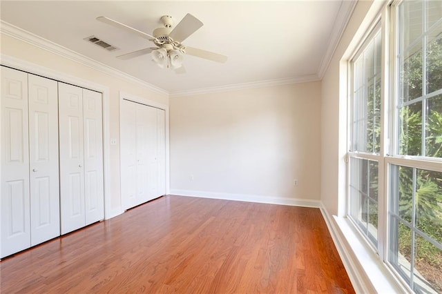 unfurnished bedroom with ceiling fan, two closets, wood-type flooring, and multiple windows