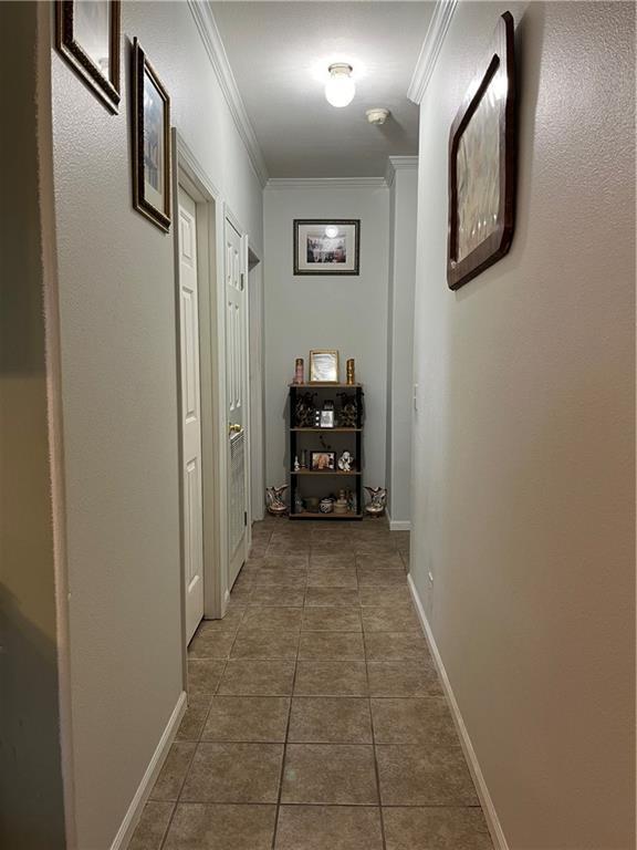 hall featuring baseboards, tile patterned flooring, and crown molding