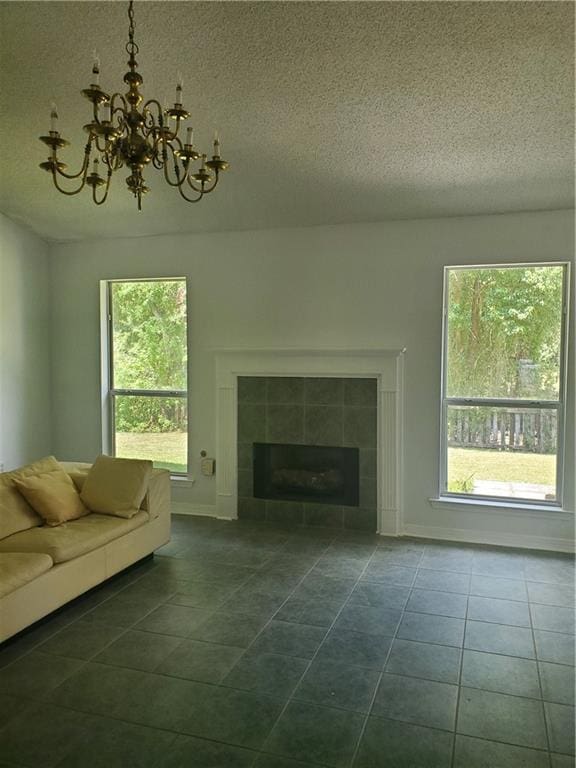 unfurnished living room with a notable chandelier, a textured ceiling, a tile fireplace, and dark tile patterned floors