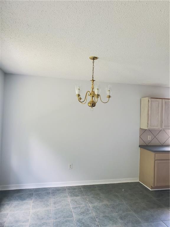 1122 Lori Dr, Slidell, LA 70461 - unfurnished dining area with a chandelier, a textured ceiling, dark tile patterned flooring, and baseboards