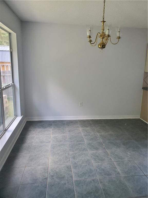 empty room with a notable chandelier and dark tile patterned flooring