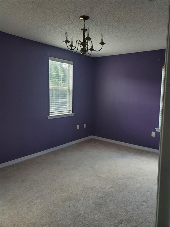 spare room featuring carpet floors, an inviting chandelier, and a textured ceiling