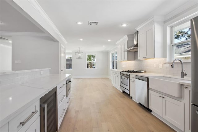 kitchen featuring light hardwood / wood-style flooring, beverage cooler, stainless steel appliances, white cabinetry, and wall chimney range hood