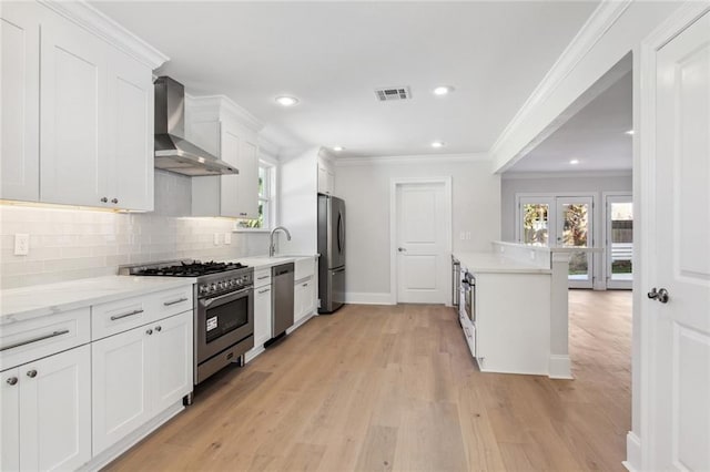 kitchen with wall chimney range hood, white cabinets, stainless steel appliances, and light hardwood / wood-style floors