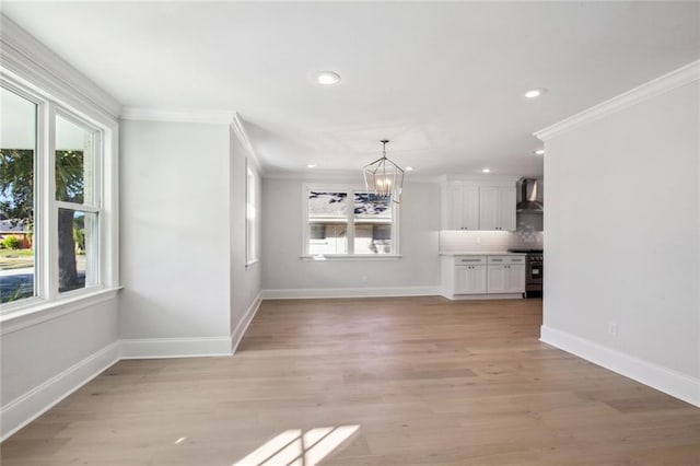 unfurnished living room with crown molding, an inviting chandelier, and light hardwood / wood-style floors