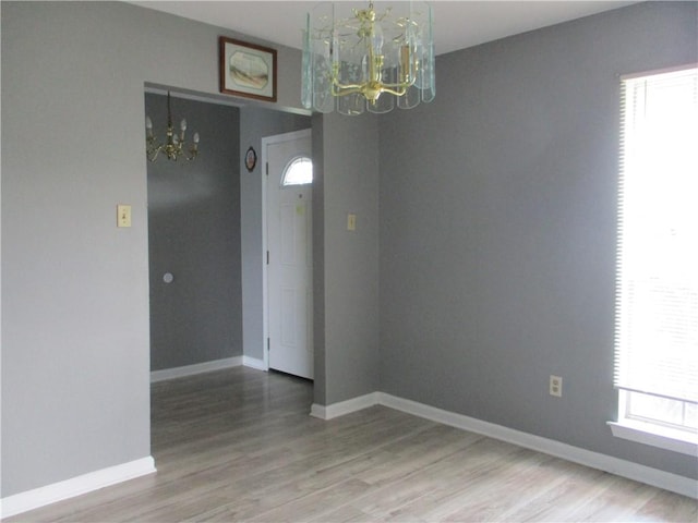 unfurnished room featuring a wealth of natural light, an inviting chandelier, and light hardwood / wood-style floors