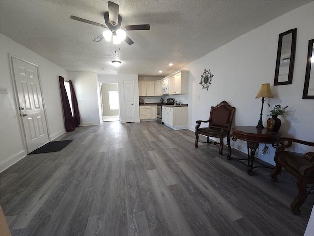 living room with a textured ceiling, ceiling fan, and dark wood-type flooring