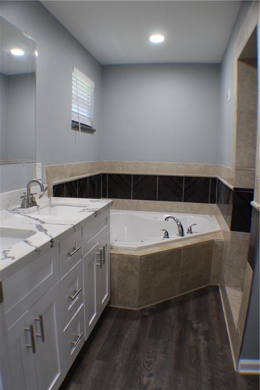 bathroom featuring wood-type flooring, tiled tub, and vanity