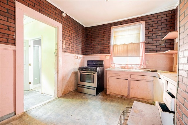 kitchen with brick wall, light brown cabinetry, light tile patterned floors, ornamental molding, and stainless steel gas stove