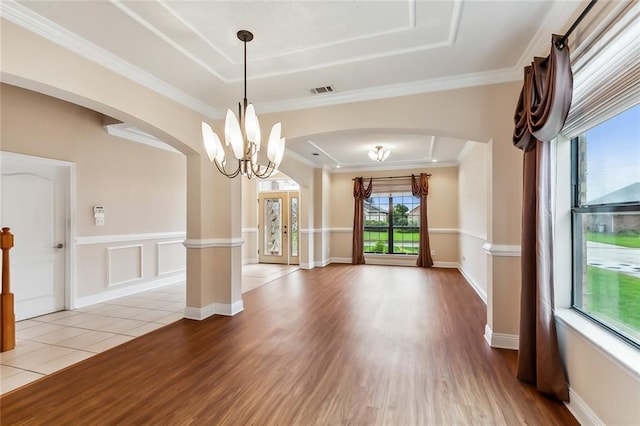 empty room featuring crown molding, light hardwood / wood-style flooring, a tray ceiling, and a notable chandelier