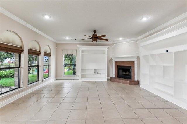 unfurnished living room featuring light tile patterned floors, a tiled fireplace, built in shelves, ceiling fan, and ornamental molding