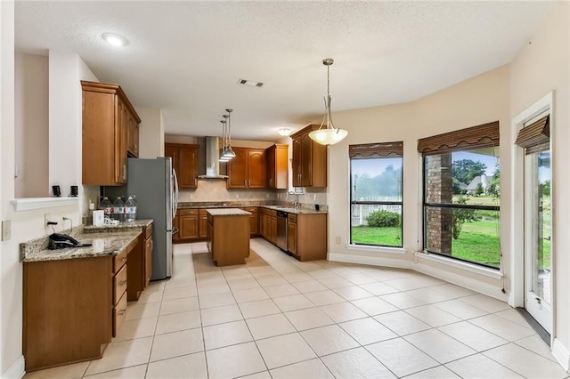 kitchen featuring light stone countertops, hanging light fixtures, stainless steel dishwasher, a center island, and wall chimney range hood