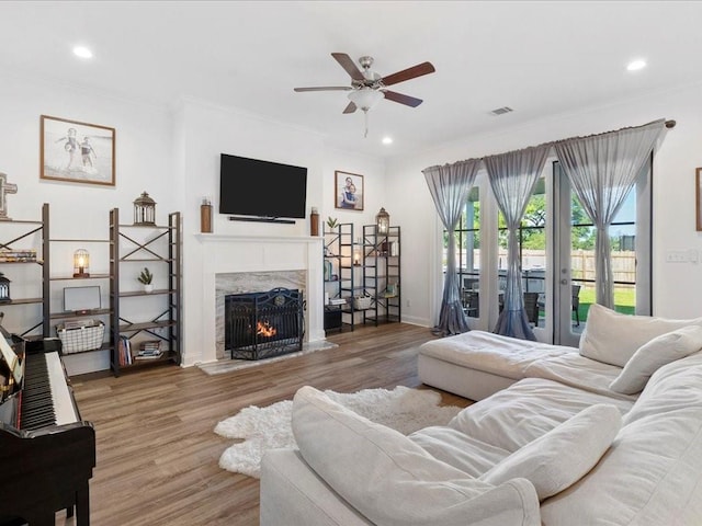 living room featuring wood-type flooring, crown molding, a high end fireplace, and ceiling fan