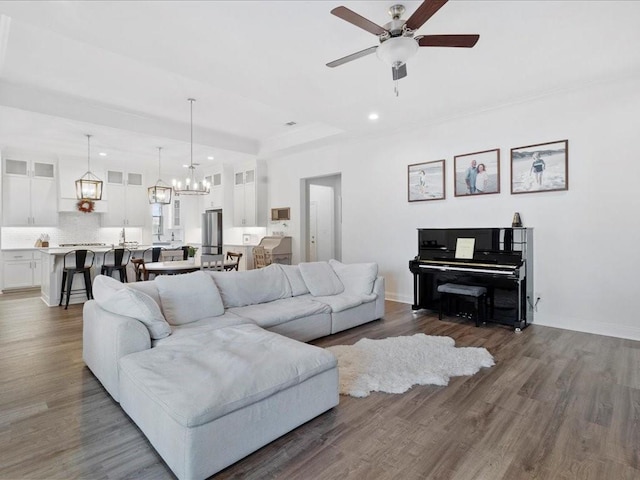 living room featuring ceiling fan with notable chandelier, wood-type flooring, and a tray ceiling