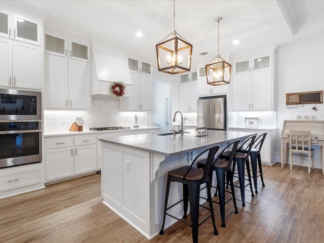 kitchen featuring a kitchen island with sink, light hardwood / wood-style flooring, sink, decorative backsplash, and appliances with stainless steel finishes