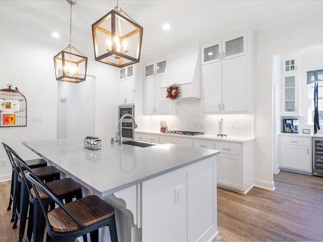 kitchen with white cabinets, backsplash, light hardwood / wood-style flooring, pendant lighting, and a kitchen island with sink