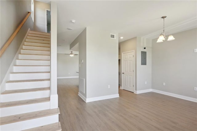 stairway with electric panel, ceiling fan with notable chandelier, and hardwood / wood-style flooring