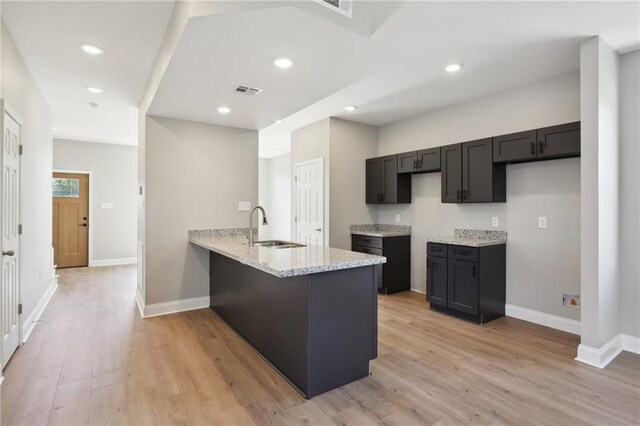 kitchen with light stone counters, sink, light wood-type flooring, and kitchen peninsula