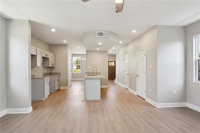 kitchen with light wood-type flooring, light stone counters, sink, an island with sink, and ceiling fan