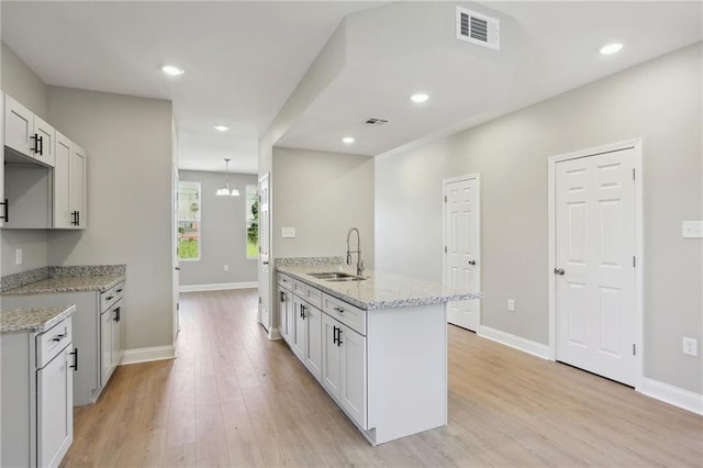 kitchen with kitchen peninsula, sink, light stone counters, light wood-type flooring, and white cabinets