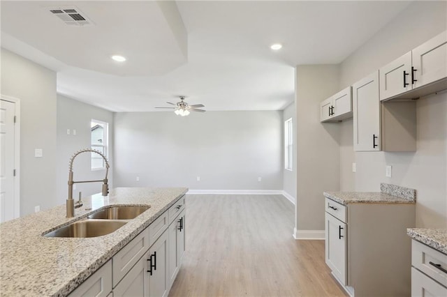 kitchen featuring white cabinets, light hardwood / wood-style flooring, light stone countertops, sink, and ceiling fan