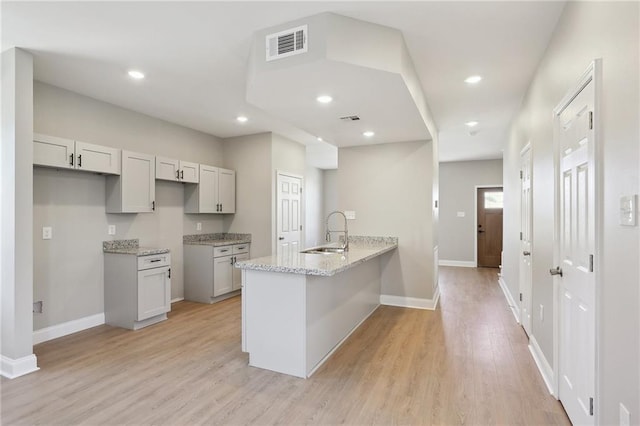 kitchen with kitchen peninsula, sink, light stone countertops, and light hardwood / wood-style floors