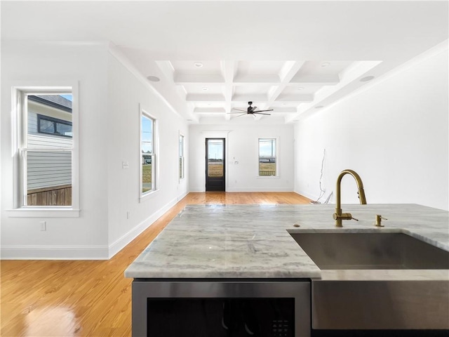kitchen with ceiling fan, beam ceiling, a sink, light wood-style flooring, and a wealth of natural light