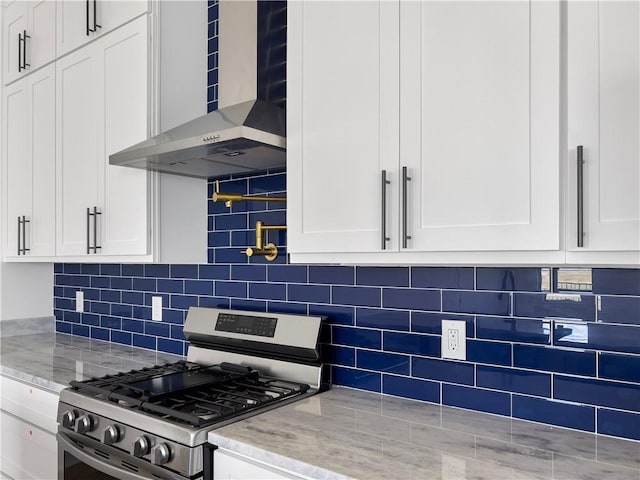 kitchen with white cabinetry, stainless steel gas range oven, wall chimney range hood, backsplash, and light stone countertops