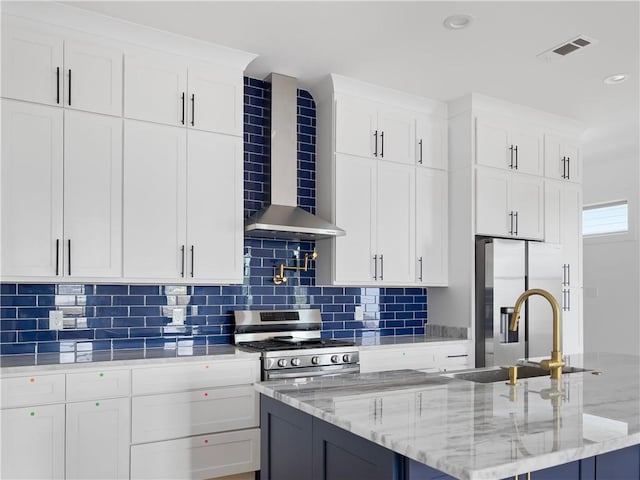 kitchen with wall chimney exhaust hood, stainless steel appliances, white cabinetry, and an island with sink