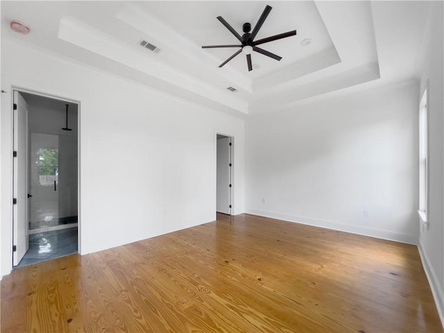 unfurnished room with visible vents, a ceiling fan, wood finished floors, and a tray ceiling