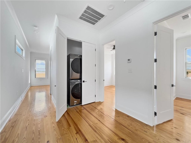 laundry room with light wood-type flooring, stacked washer and clothes dryer, crown molding, and ceiling fan