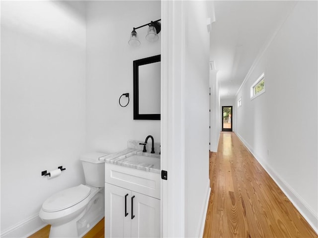 half bathroom featuring toilet, baseboards, wood finished floors, and vanity