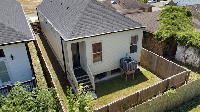 back of property with a fenced backyard, roof with shingles, and a yard