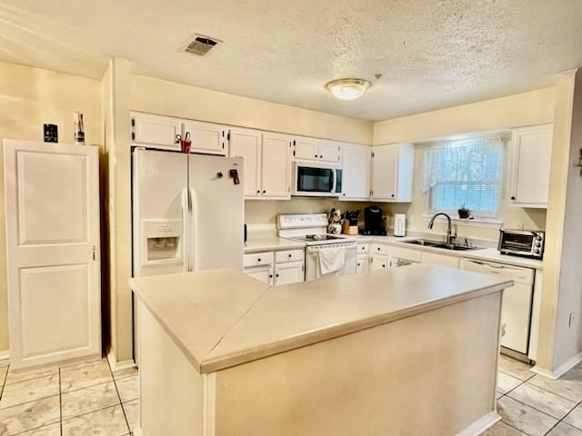 kitchen with sink, a center island, a textured ceiling, white appliances, and white cabinets