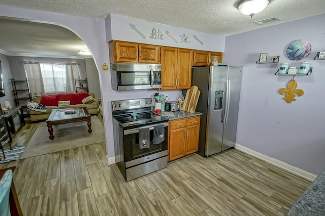 kitchen with arched walkways, appliances with stainless steel finishes, light wood-type flooring, and visible vents