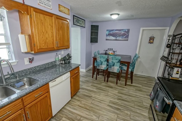 kitchen featuring brown cabinetry, white dishwasher, a textured ceiling, a sink, and light wood-type flooring