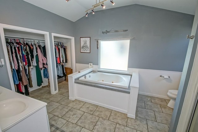 bathroom featuring tile patterned floors, vanity, rail lighting, lofted ceiling, and a bathtub