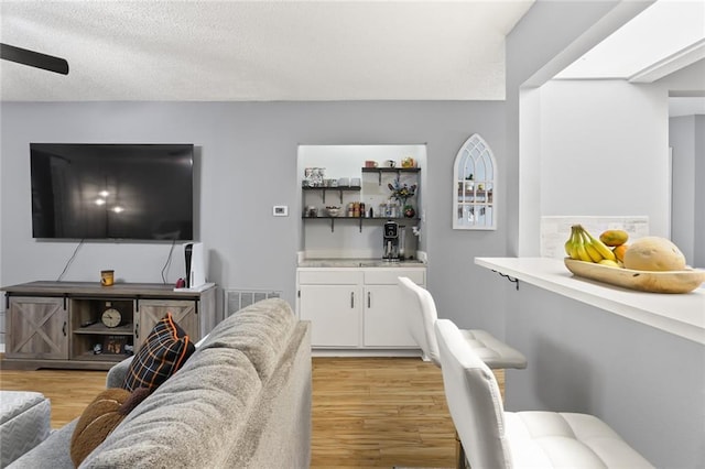 bar with a textured ceiling, light hardwood / wood-style flooring, and white cabinets