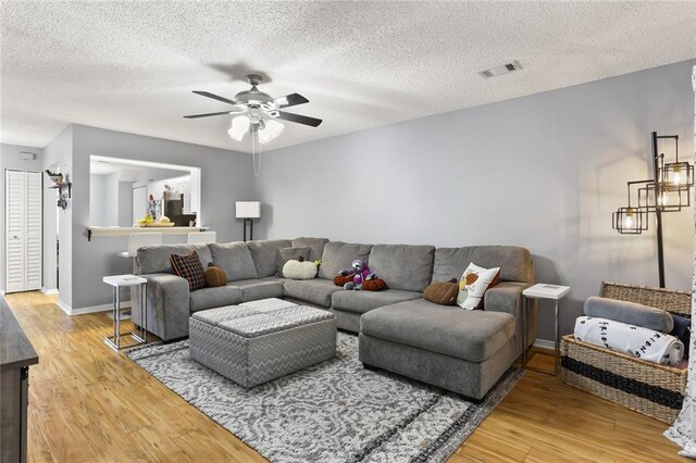 living room featuring light wood-type flooring, ceiling fan, and a textured ceiling