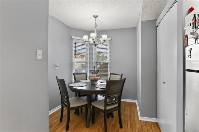 dining area featuring a textured ceiling, light hardwood / wood-style flooring, and a chandelier