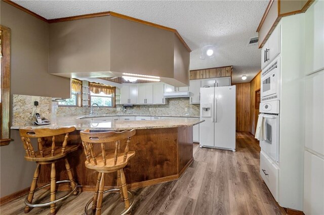 kitchen featuring a textured ceiling, a kitchen breakfast bar, white appliances, hardwood / wood-style floors, and kitchen peninsula