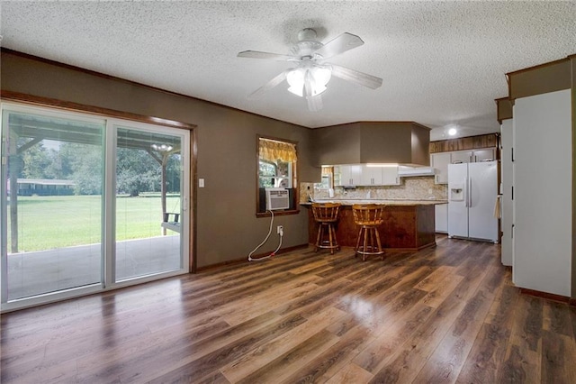 kitchen featuring dark hardwood / wood-style flooring, kitchen peninsula, a breakfast bar area, white fridge with ice dispenser, and tasteful backsplash