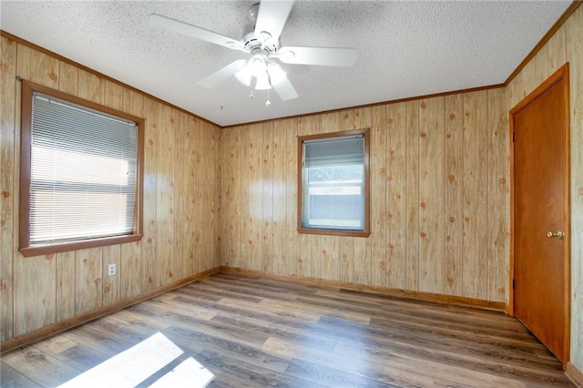 empty room with a textured ceiling, light hardwood / wood-style flooring, ceiling fan, and wooden walls