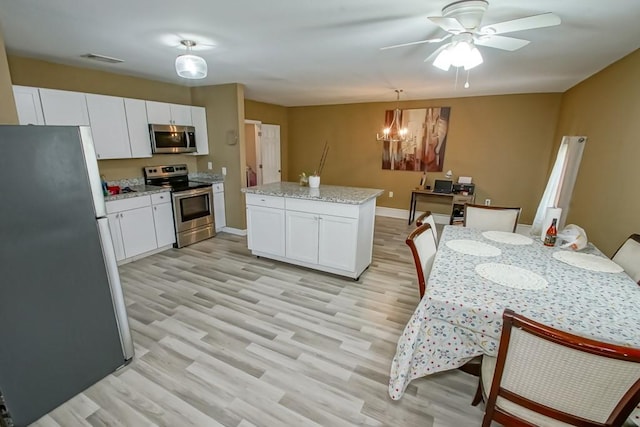 kitchen featuring light hardwood / wood-style flooring, light stone counters, decorative light fixtures, and appliances with stainless steel finishes