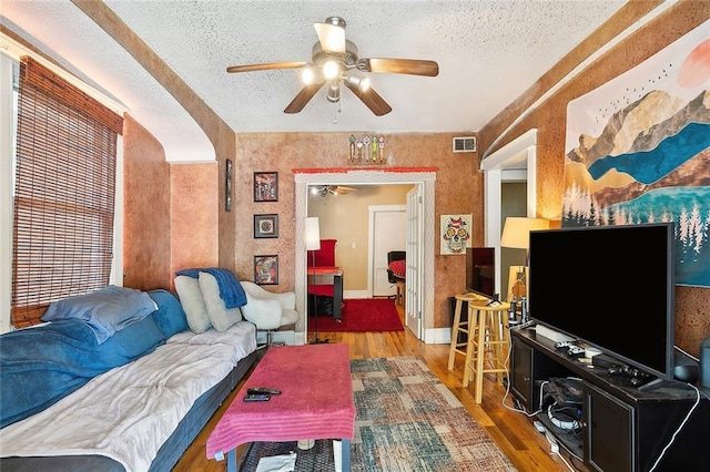 living room with a textured ceiling, ceiling fan, and hardwood / wood-style flooring